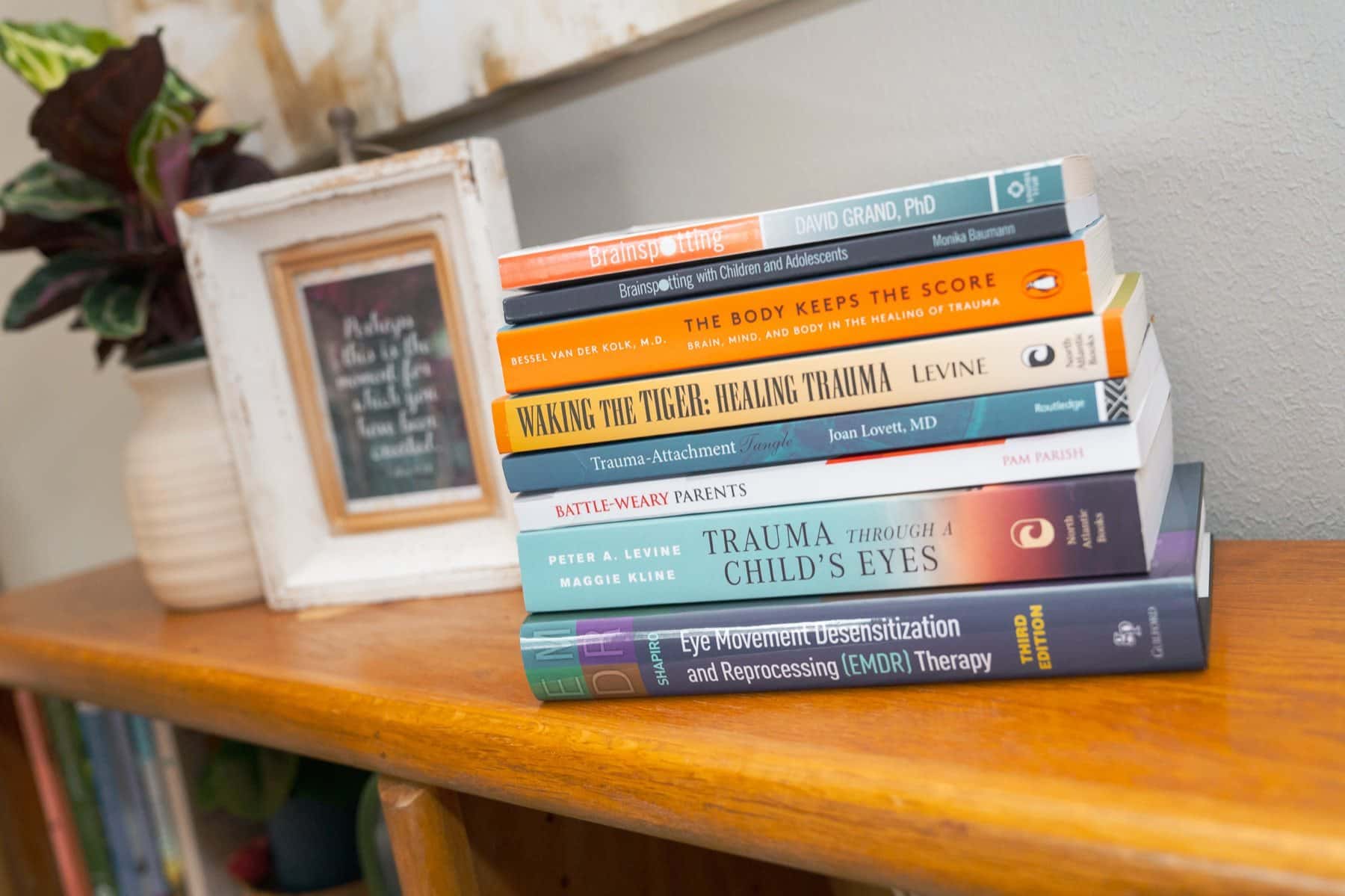 A stack of well-read trauma and counseling books on a wooden shelf in the Texarkana Counseling Collective office.